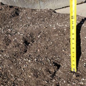 Close-up of dark soil on the ground with a yellow measuring tape marking depth.