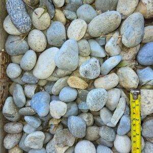 Close-up of smooth gray and beige pebbles with a yellow measuring tape along the right edge