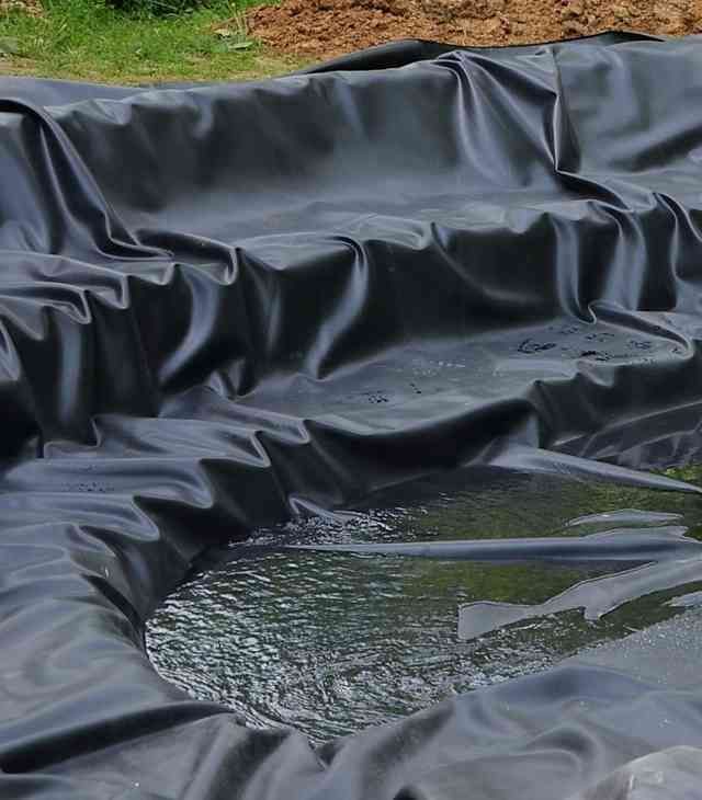 Black pond liner with a shallow pool of water in a grassy outdoor area