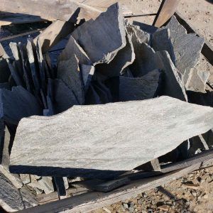 Stack of gray slate stone slabs on a rough outdoor ground