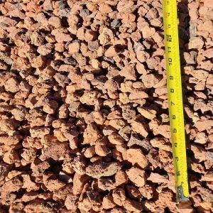 Close-up of brown gravel beside a yellow measuring tape showing scale.