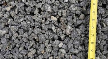 Pile of gray gravel stones with a yellow measuring tape along the right edge.