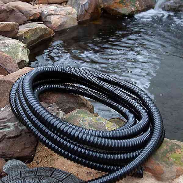 Coiled black corrugated hose lying on rocks beside a pond or stream