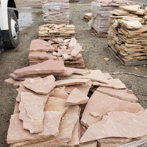 Stacks of flat pink stone slabs piled outdoors on a gravel lot near a vehicle.