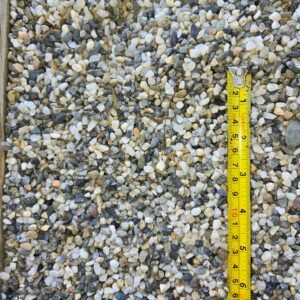 Close-up of light gray gravel with a yellow measuring tape along the right edge.