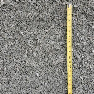 Close-up of gray gravel with a yellow measuring tape along the right edge.