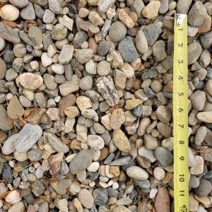 Close-up of mixed pebbles and gravel with a yellow measuring tape along the right edge.