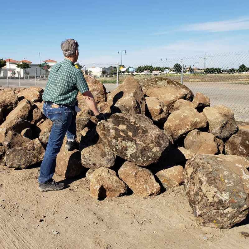 Person in a green shirt stacking large rocks outdoors near a field