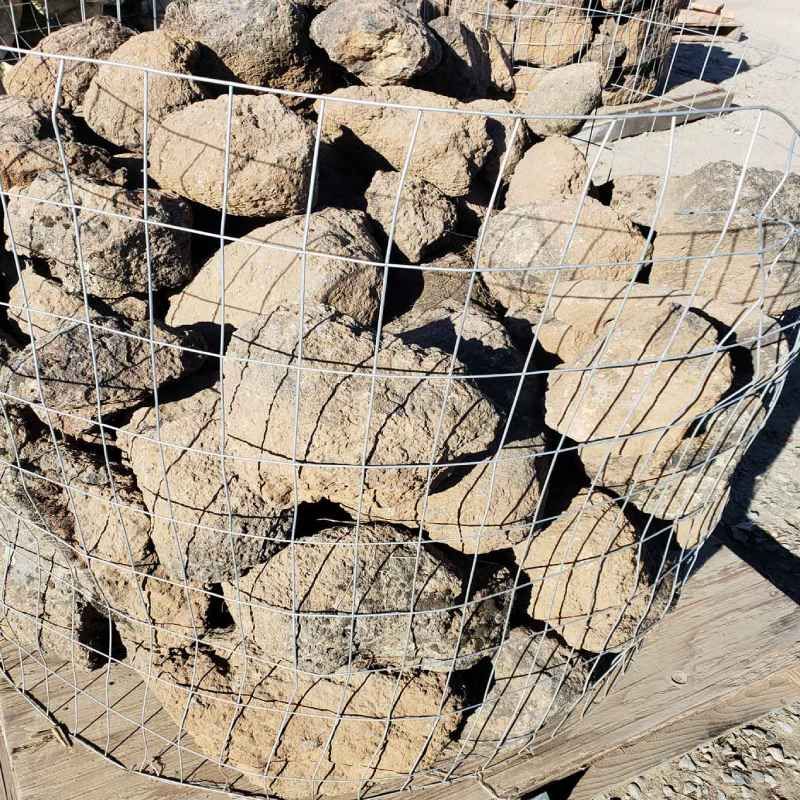Wire mesh cage filled with large tan rocks, stacked outdoors on a wooden pallet