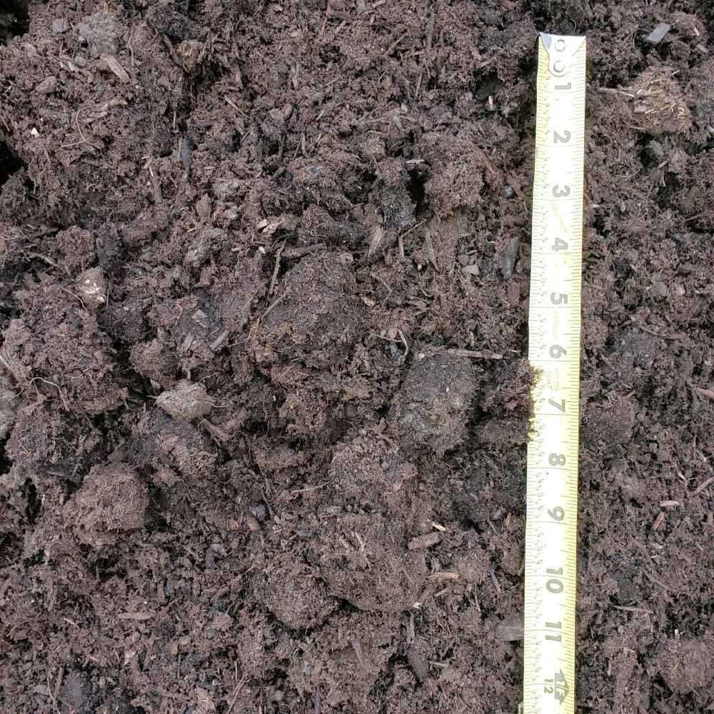 Close-up of dark, crumbly soil beside a white measuring ruler.
