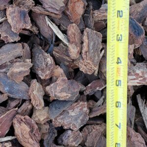 Close-up of brown mulch pieces beside a yellow measuring tape showing scale.