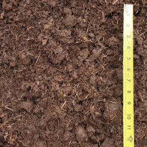 Close-up of brown mulch or soil with a yellow measuring tape along the right edge.