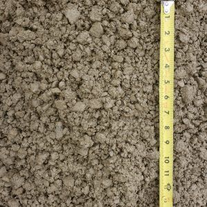 Close-up of brown soil or granular material beside a yellow measuring tape in inches