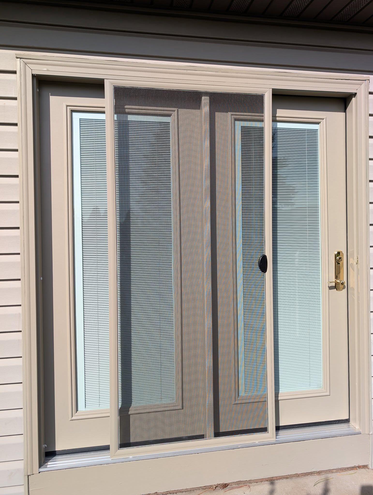 A beige double door with a light-colored retractable screen door installed, set against horizontal tan siding.