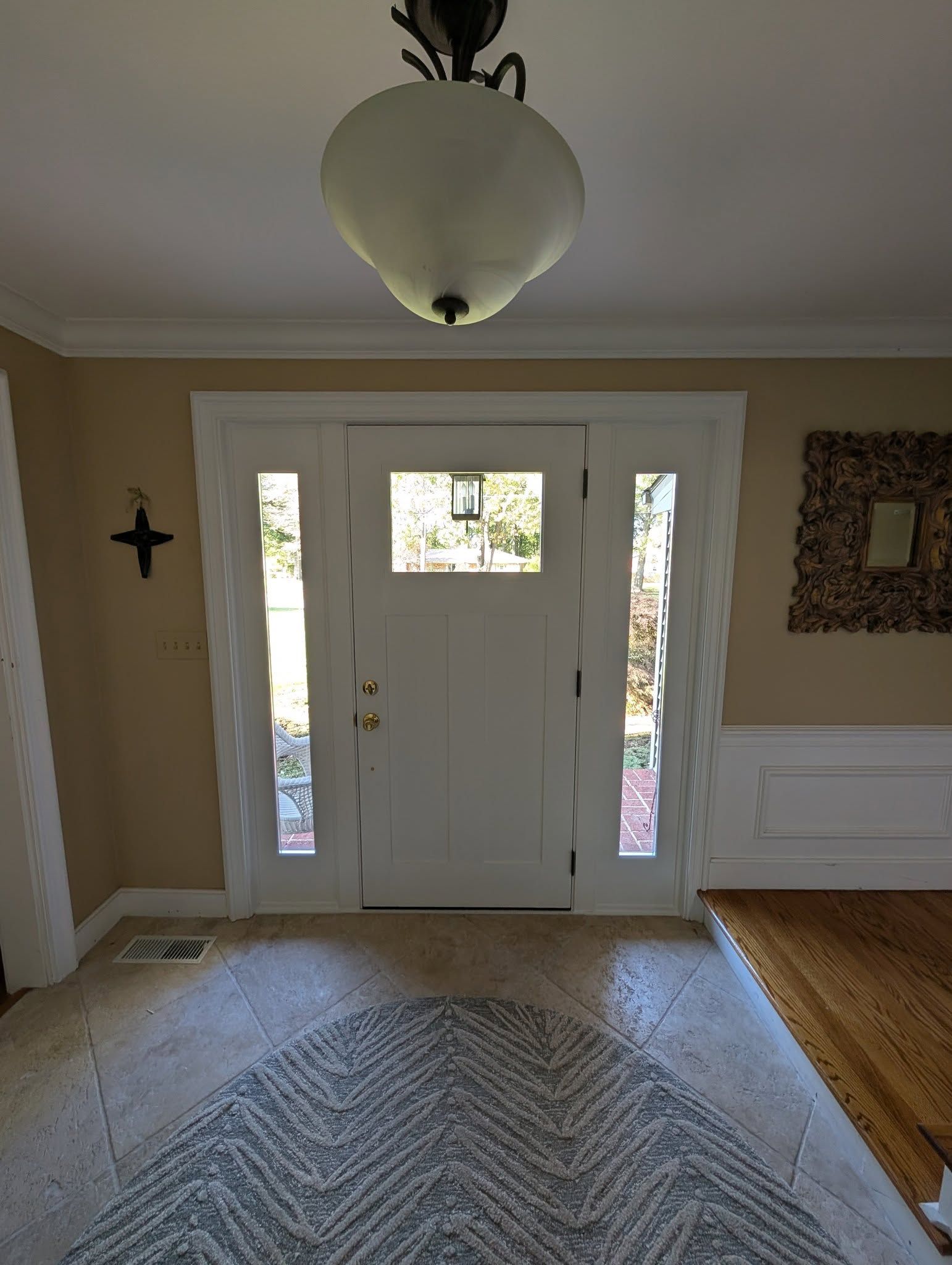 A front entryway with a white door, side windows, a pendant light, a patterned rug, and beige walls with white trim.