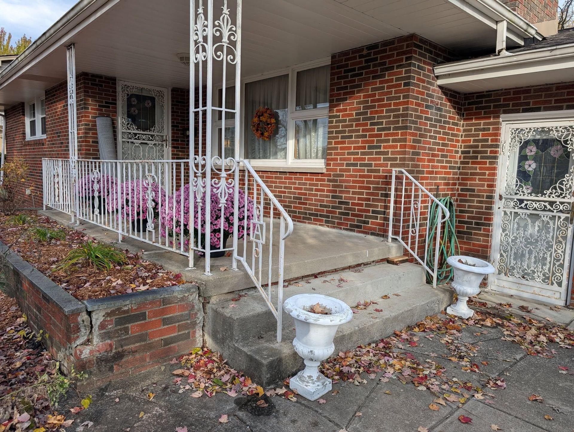 A brick house exterior with a white porch railing, steps, two white planters, and a storm door decorated for autumn.