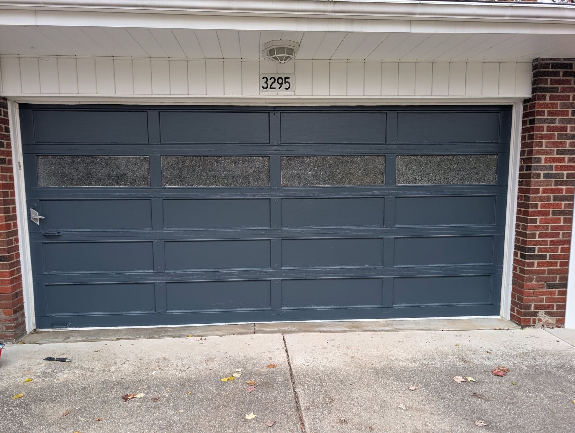 A dark gray four-panel garage door with textured windows above a concrete driveway, set between two brick walls.