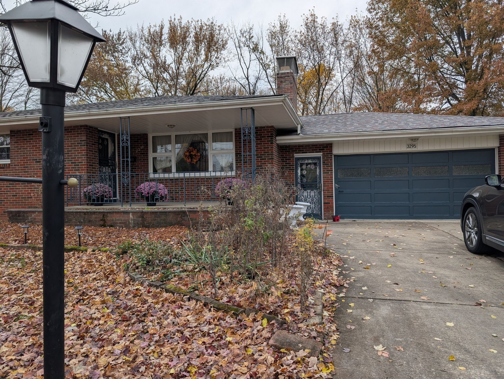 A single-story brick house with a covered porch, an attached garage, and a lamppost in the foreground on an autumn day.