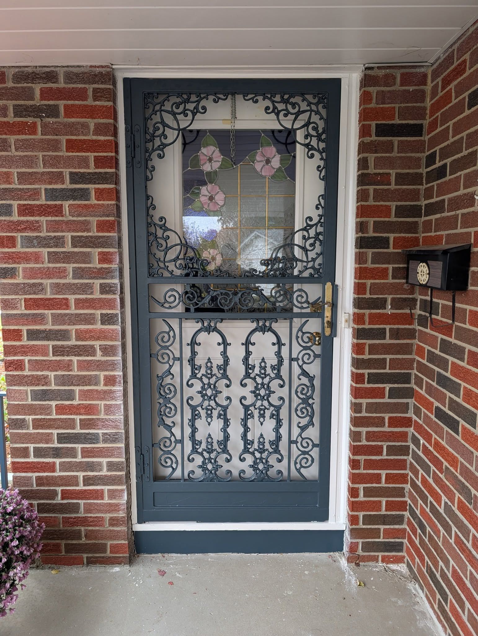 A grey ornate metal security screen door set against a red brick house entrance.