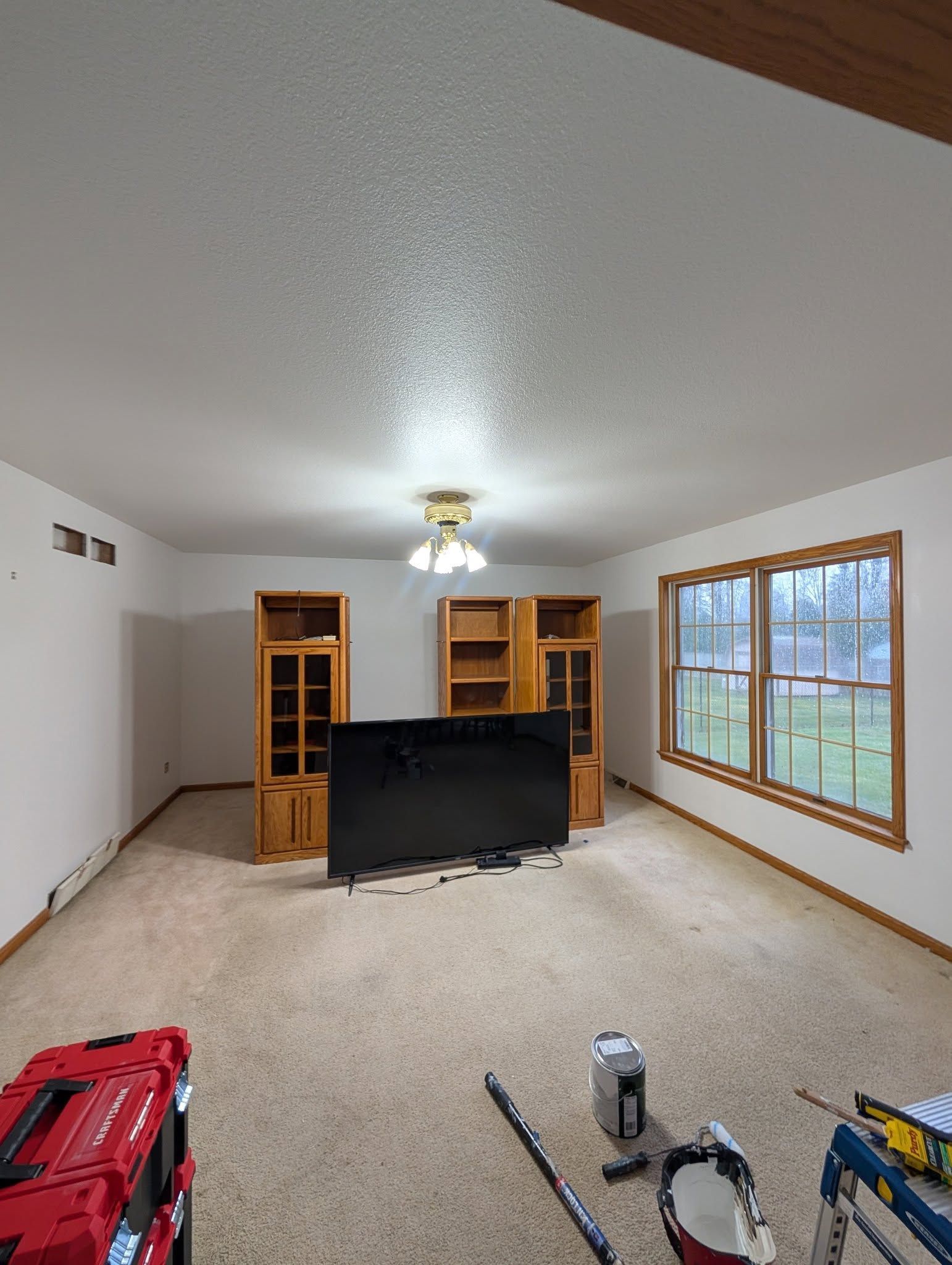 A room under renovation with a flat-screen TV and wooden shelving units in the center, and construction tools on the carpet.