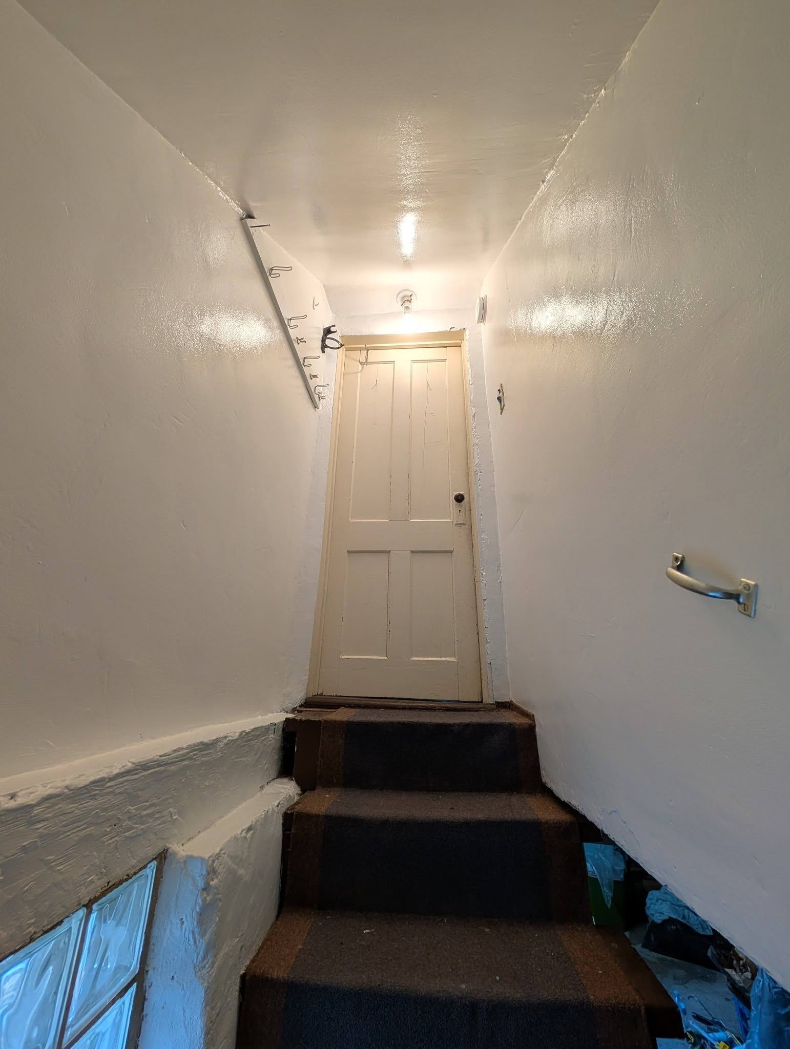 A set of dark, carpeted stairs leading up to a closed, light-colored wooden door in a narrow, white-walled hallway.