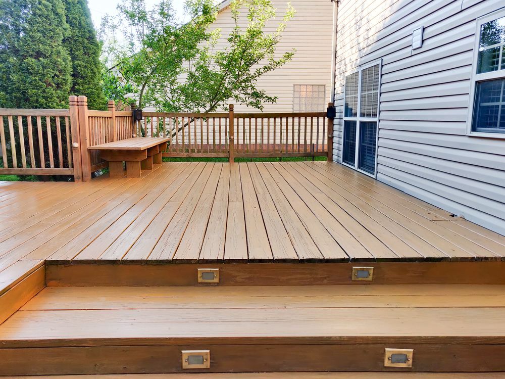 A wooden deck with two steps, recessed lighting, and a railing, attached to a house with white horizontal siding.