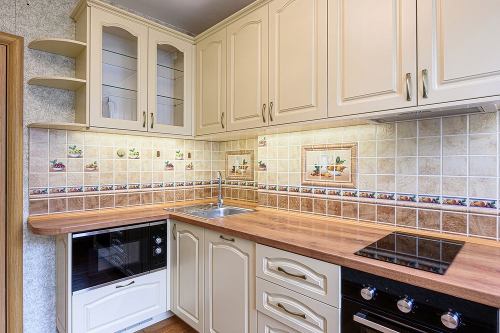 A bright kitchen with cream-colored cabinets, wood-tone countertops, tiled backsplash, and built-in appliances.