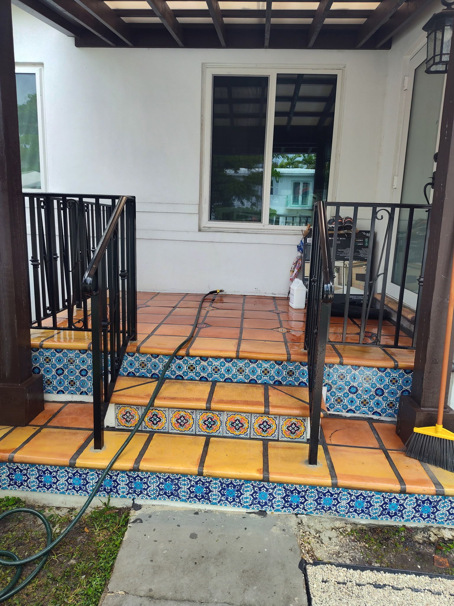 Front porch with orange terracotta tiles, decorative blue and white patterned risers, and black iron railings.