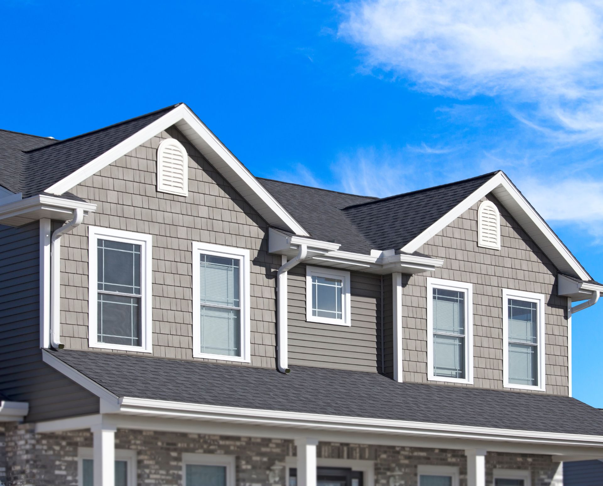 Two-story house with gray siding, white trim, dark roof, and blue sky background.