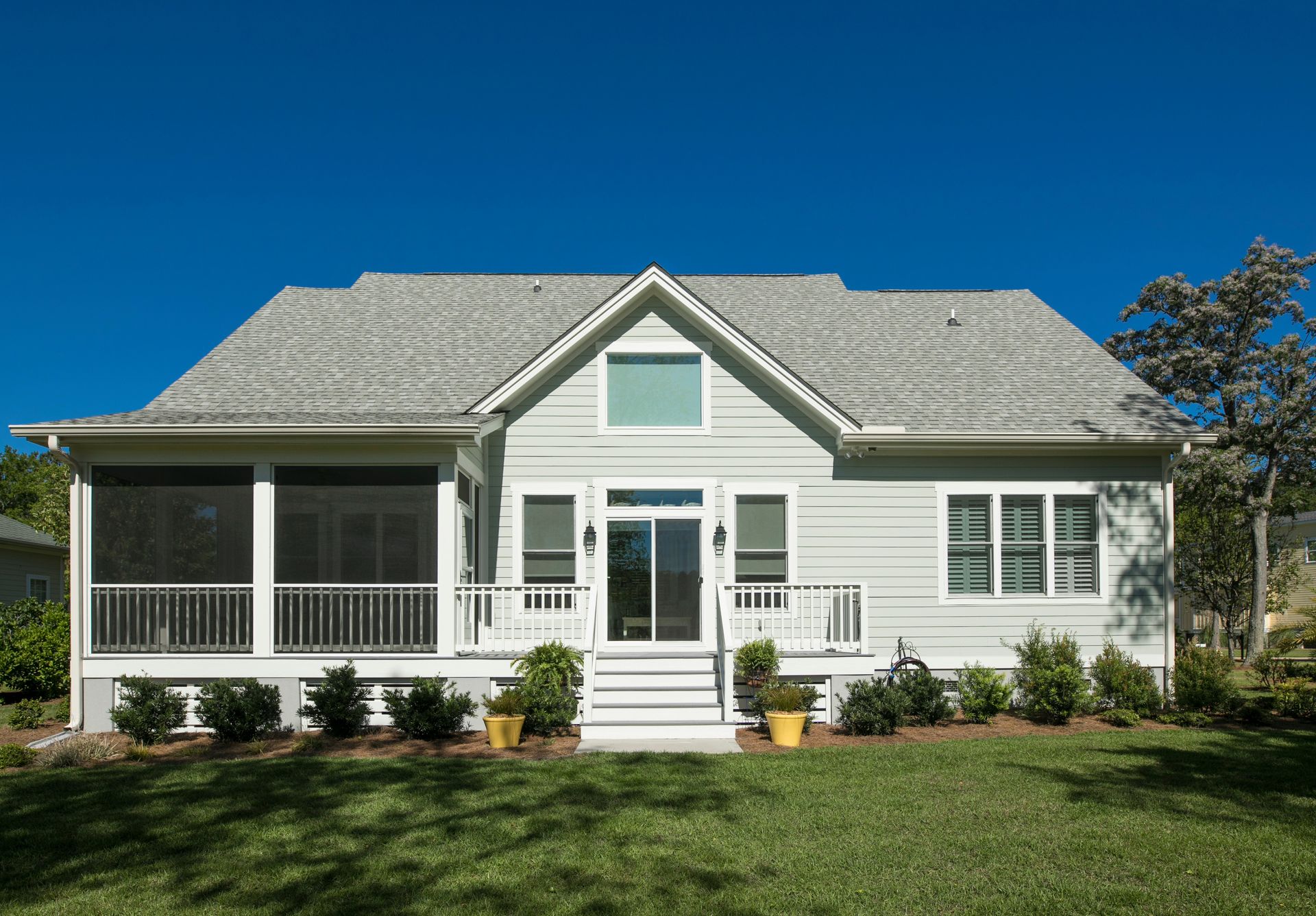 Light blue house with white trim, porch, and a screened-in area; bright blue sky.