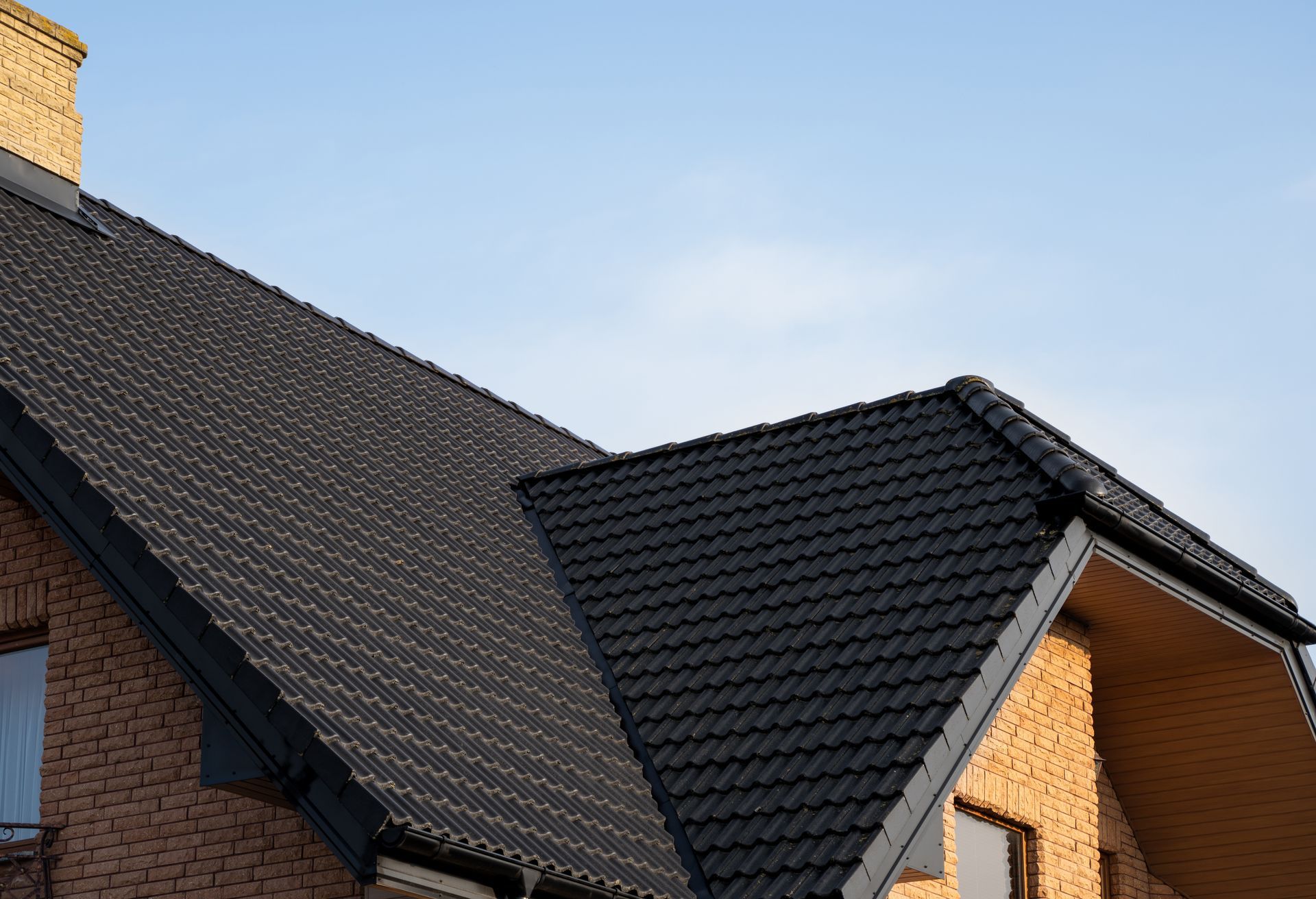 Black tiled roof on a brick building against a blue sky.