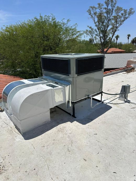 Two men are working on an air conditioner on the roof of a building.