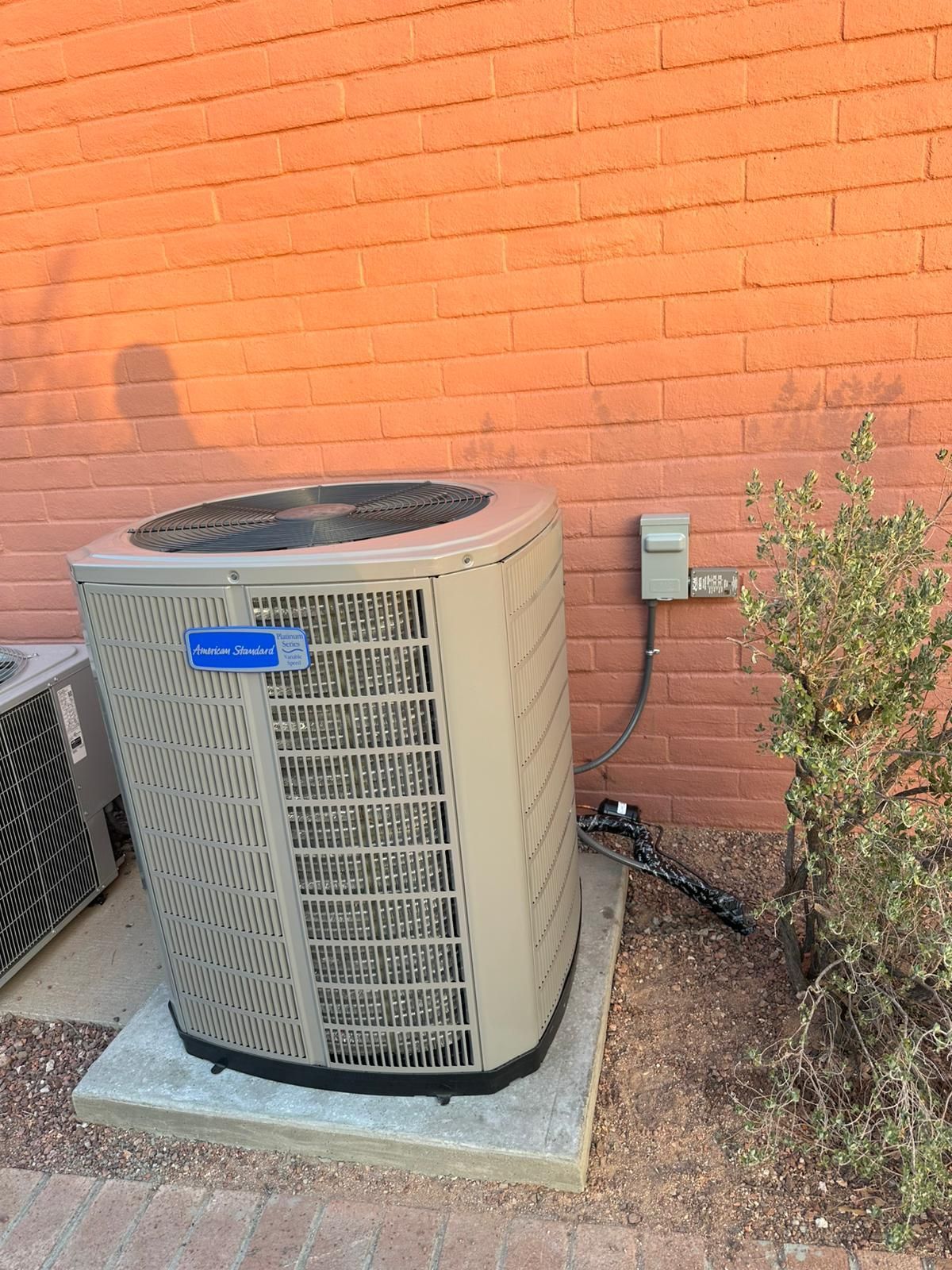 A large air conditioner is sitting outside of a brick building.