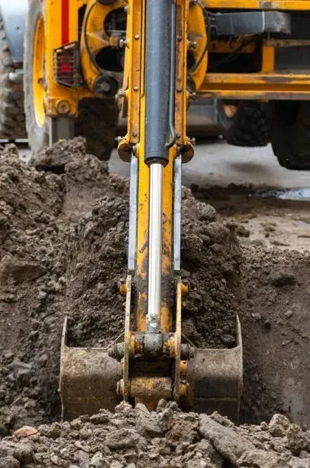 A yellow excavator bucket digging into dark soil at a construction site — Copp & Co Civil Plant Hire in Proserpine, QLD