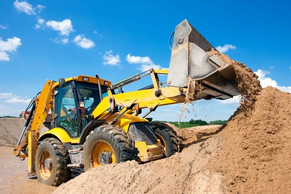 A Yellow Backhoe Loader Dumping a Scoop of Sand Onto a Large Pile — Copp & Co Civil Plant Hire in Bowen, QLD