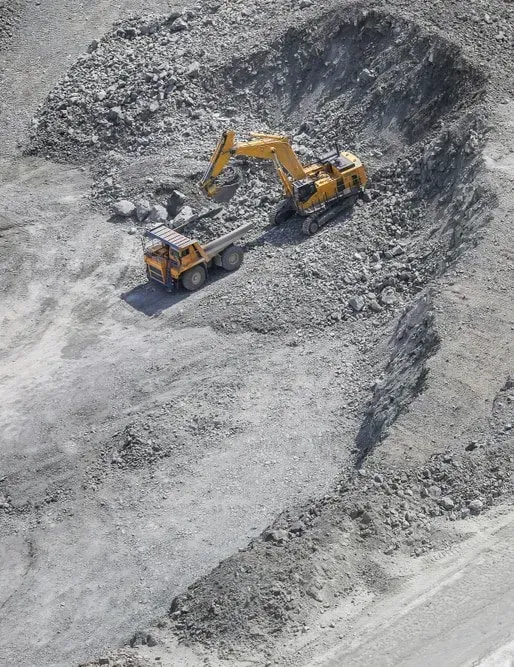 A Yellow Excavator Loading Rocky Earth Into a Dump Truck — Copp & Co Civil Plant Hire in Airlie Beach, QLD