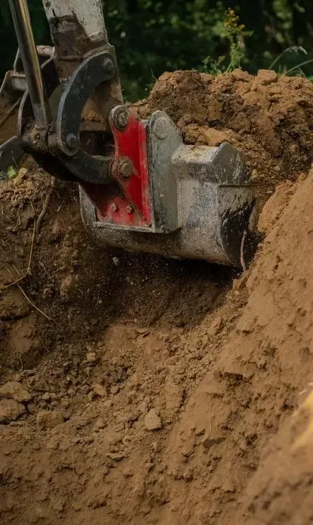 A Mechanical Excavator Bucket Digging Into Brown Soil — Copp & Co Civil Plant Hire in Airlie Beach, QLD