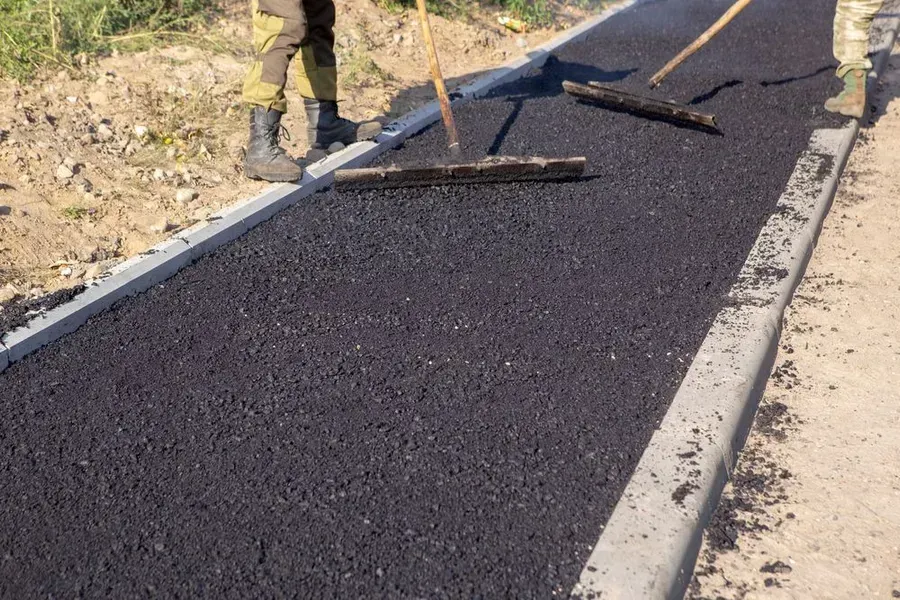 Two Workers Use Wooden Rakes to Spread Fresh Black Asphalt — Copp & Co Civil Plant Hire in Mount Julian, QLD