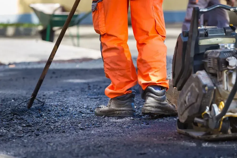A Construction Worker in Orange Pants Uses a Rake to Spread Fresh Asphalt — Copp & Co Civil Plant Hire in Mount Julian, QLD