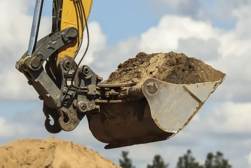 A Yellow Excavator Bucket Filled With Dirt is Held in the Air — Copp & Co Civil Plant Hire in Airlie Beach, QLD