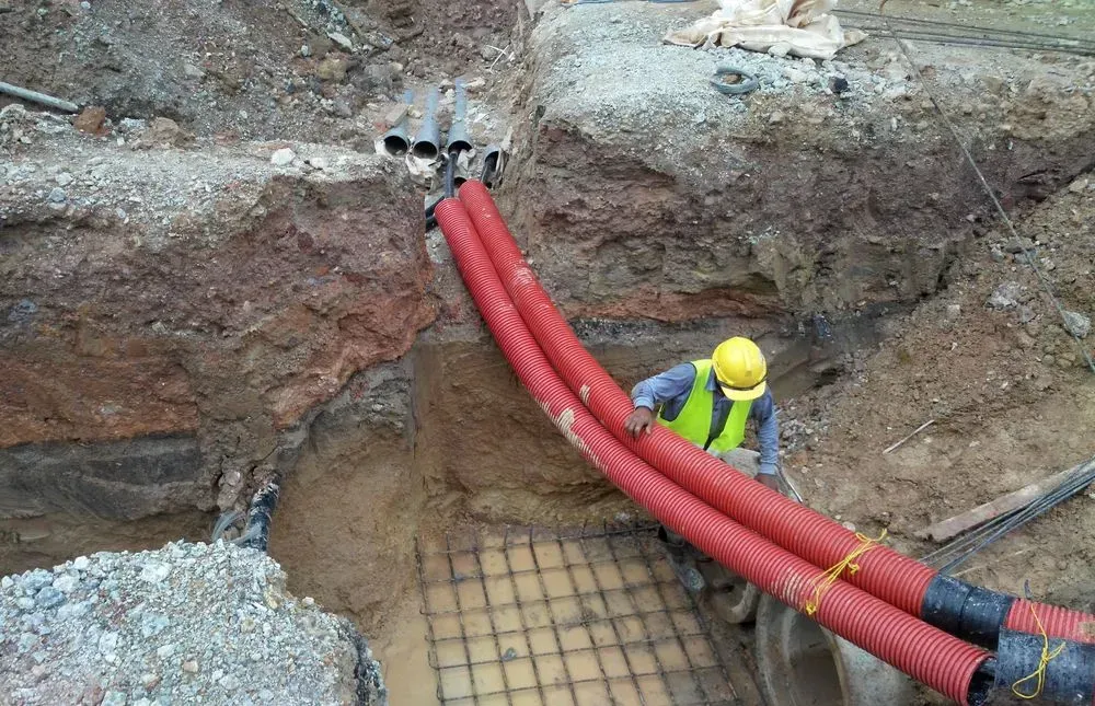 A Worker in a Yellow Vest and Hard Hat Sits in a Deep Trench — Copp & Co Civil Plant Hire in Bowen, QLD