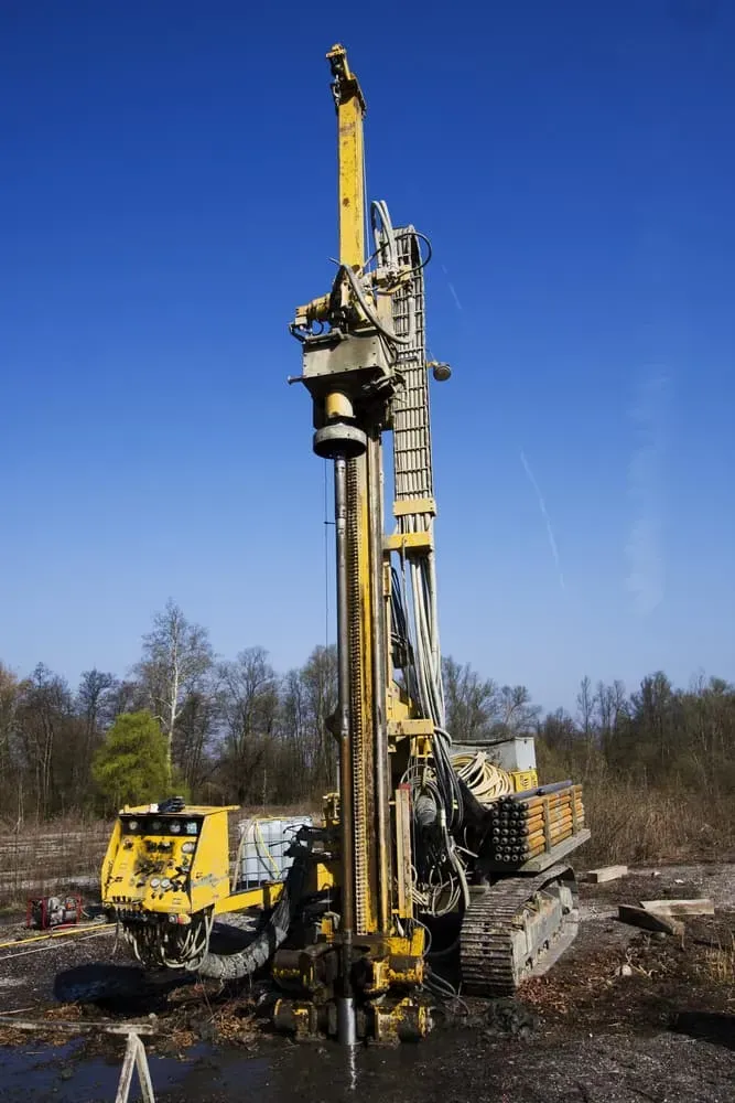 A Yellow, Tracked Drilling Rig Stands in a Field Against a Clear Blue Sky — Copp & Co Civil Plant Hire in Mount Julian, QLD