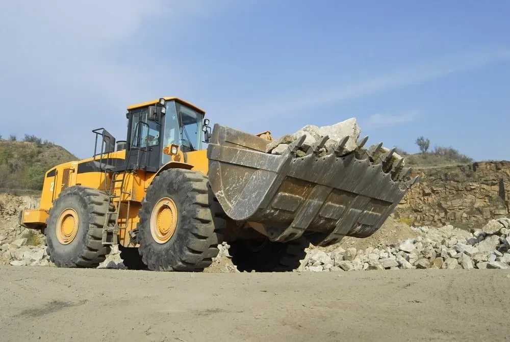 A Yellow Front-end Loader Moves Rocks in a Quarry Under a Clear Blue Sky — Copp & Co Civil Plant Hire in Mount Julian, QLD