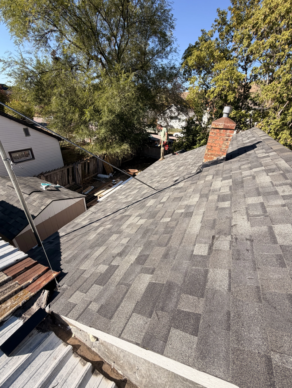 Gray shingled rooftop with brick chimney, surrounded by trees and neighboring houses