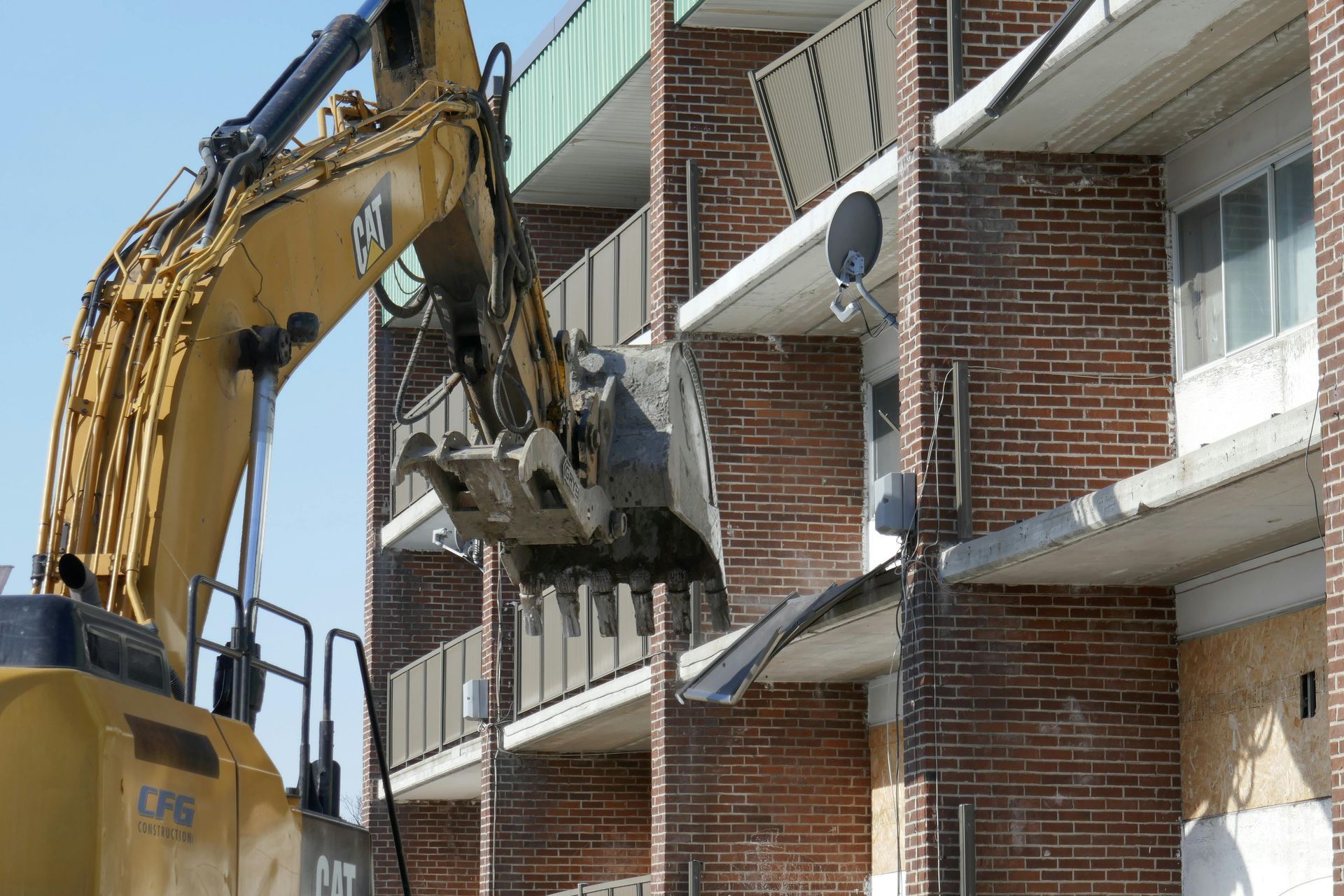 Excavator demolishing the side of a brick apartment building with balconies and air conditioners