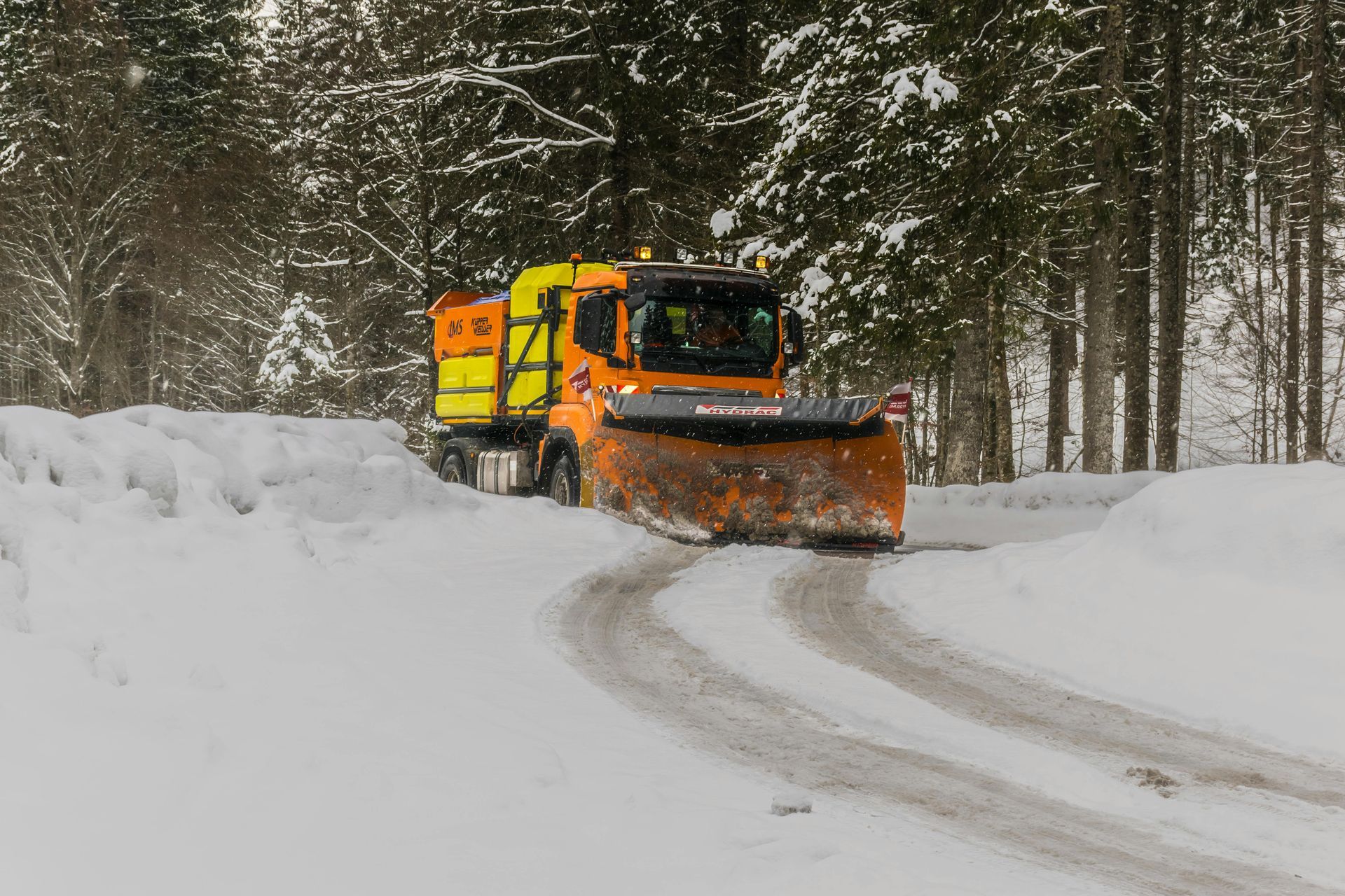 Orange snowplow clearing a snowy forest road in winter