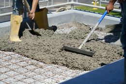 Workers smoothing wet concrete in a construction area with a rake and boots