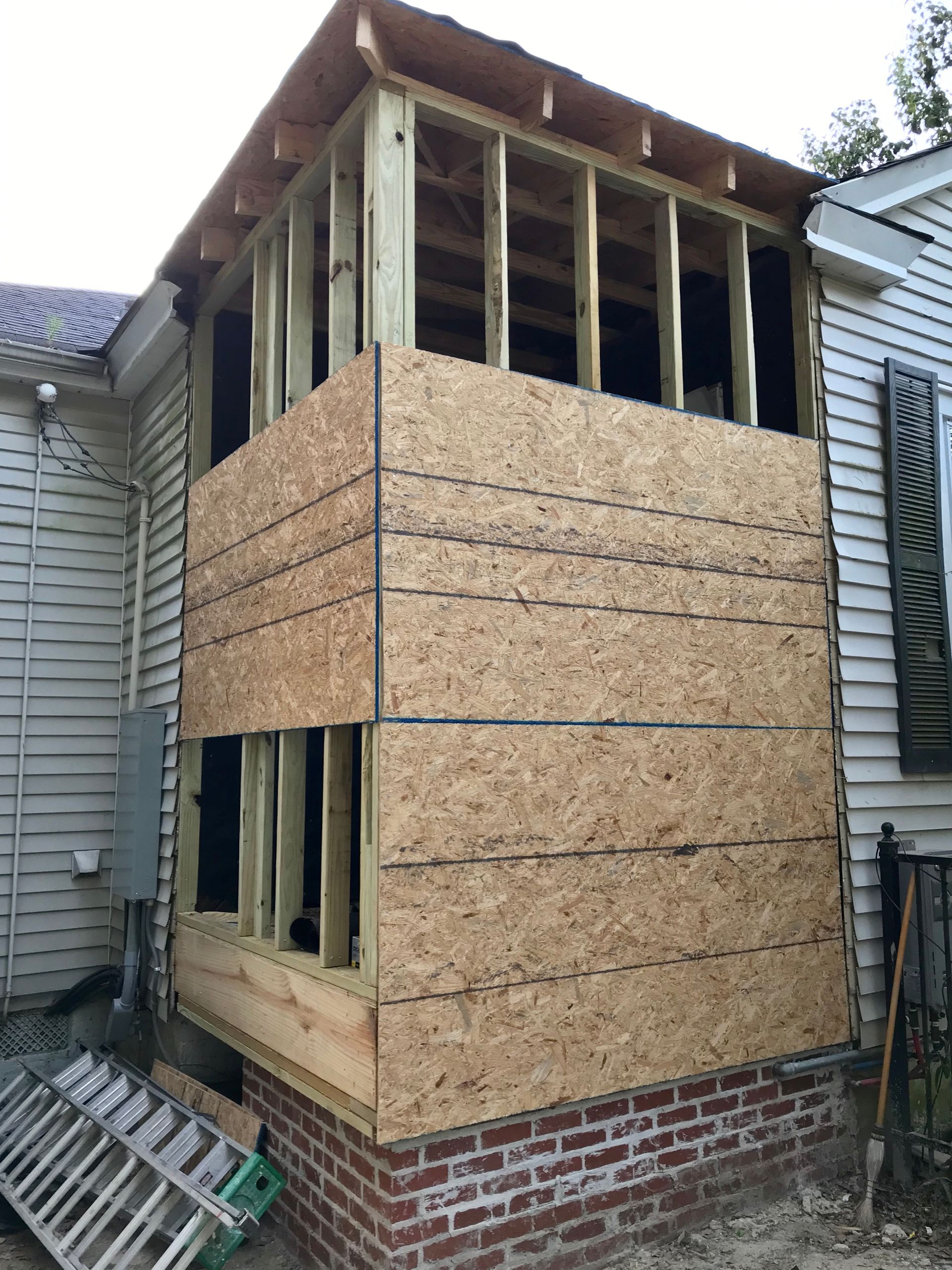 Partially rebuilt house with exposed framing, OSB siding, and brick foundation wall