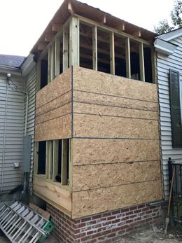 Partially rebuilt house with exposed framing, OSB siding, and brick foundation wall