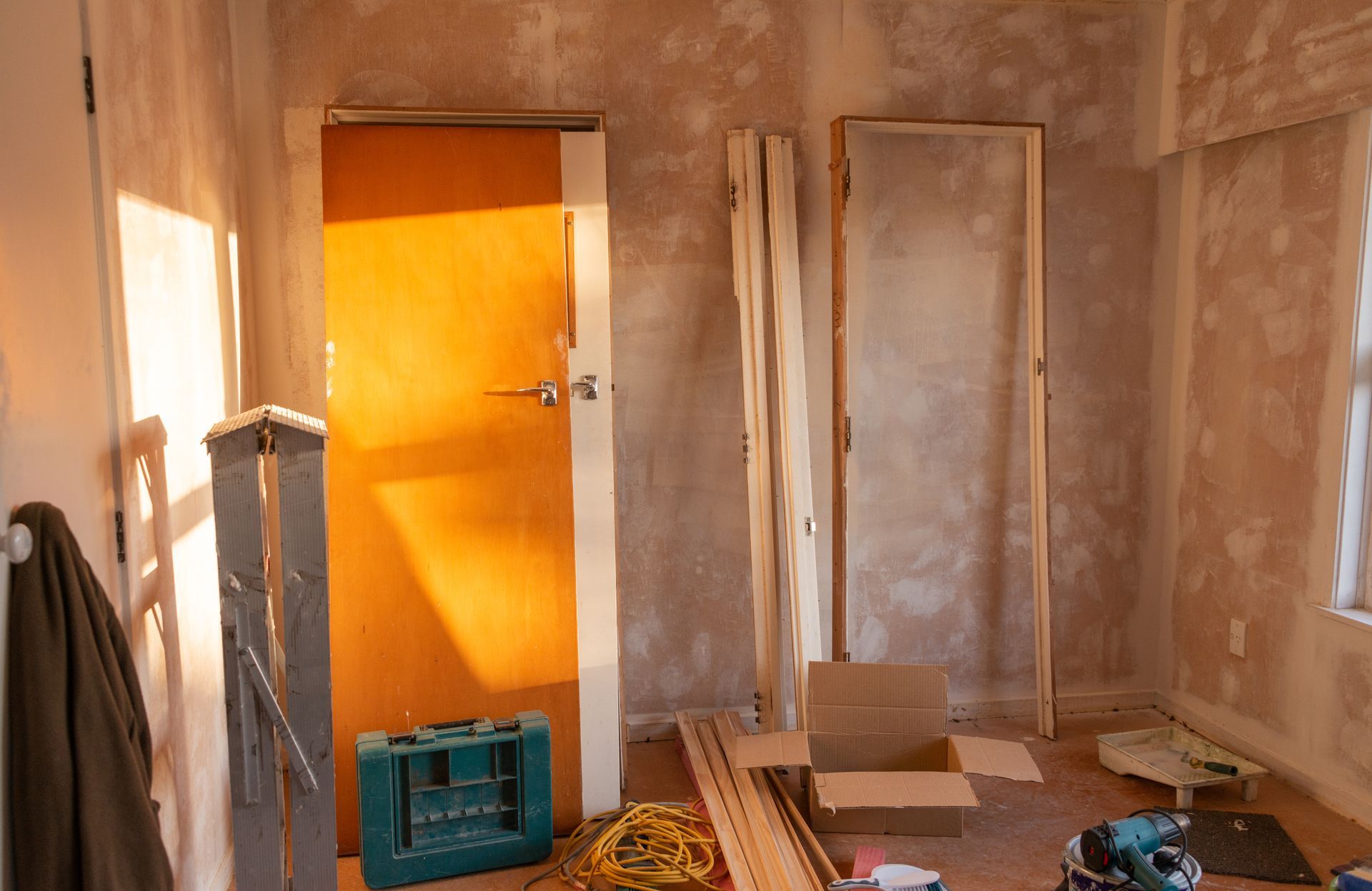 Unfinished room with exposed drywall, an orange door, and construction materials on the floor.